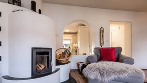 Una sala de estar con chimenea, un sofá gris con un cojín rojo y una alfombra estampada.