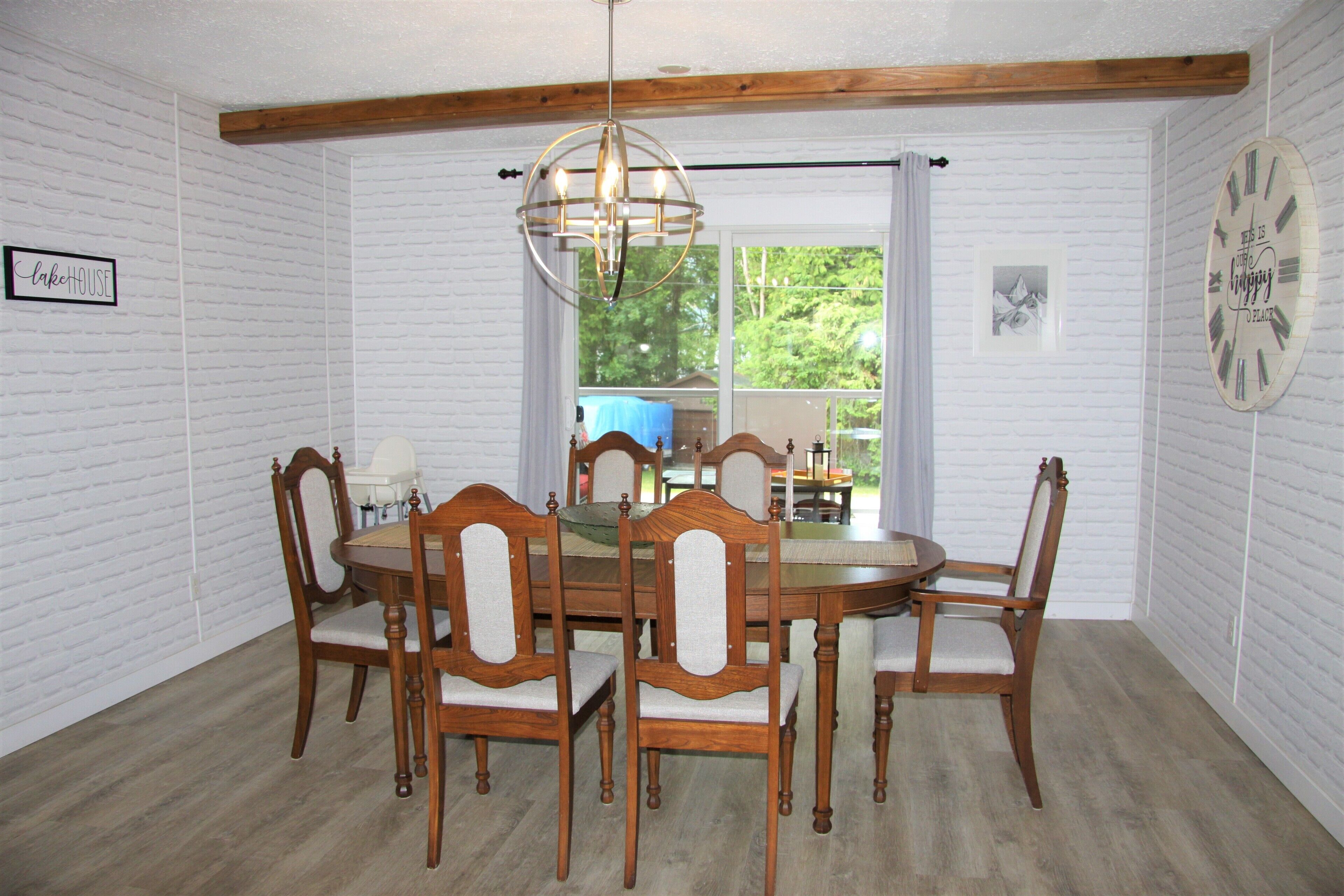 A dining room with a wooden table and chairs, a chandelier, and a clock on the wall.