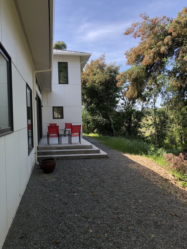A modern building with a patio area featuring red chairs and a large pot.