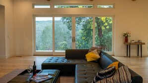 A modern living room with a sectional sofa, a coffee table, and a view of a forest through large windows. - Wake Up in Your Own Private Vineyard - Healdsburg (Healdsburg)