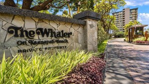 A stone wall with "The Whaler On Kaanapali Beach PRIVATE PROPERTY" signage, surrounded by greenery and a pathway leading to a building. - BeachFront Luxury 1BR Excellent Views Pool-Whaler 859 (Lahaina)