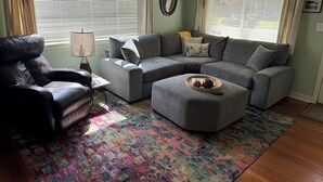 Una sala de estar con un sofá modular, un sillón de cuero, una mesa de centro y un tapete estampado.