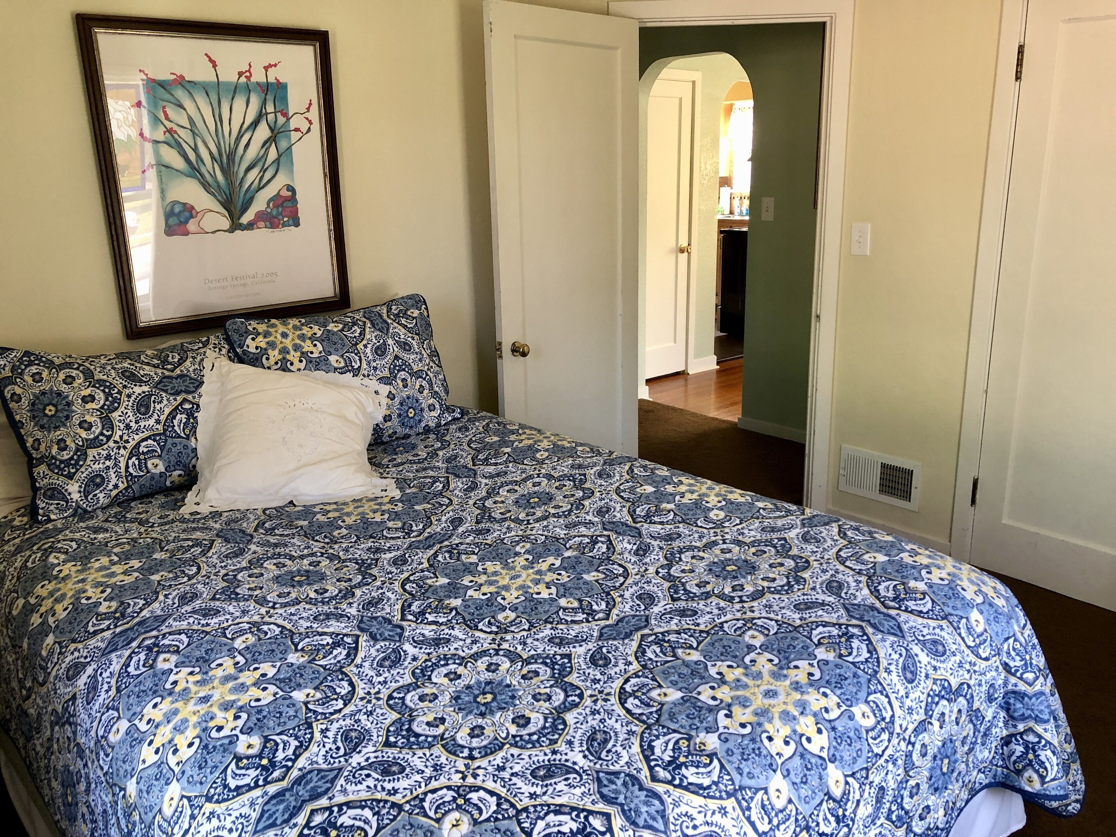 A bedroom with a patterned bedspread, a framed picture on the wall, and a door leading to another room.