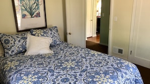 A bedroom with a patterned bedspread, a framed picture on the wall, and a door leading to another room.