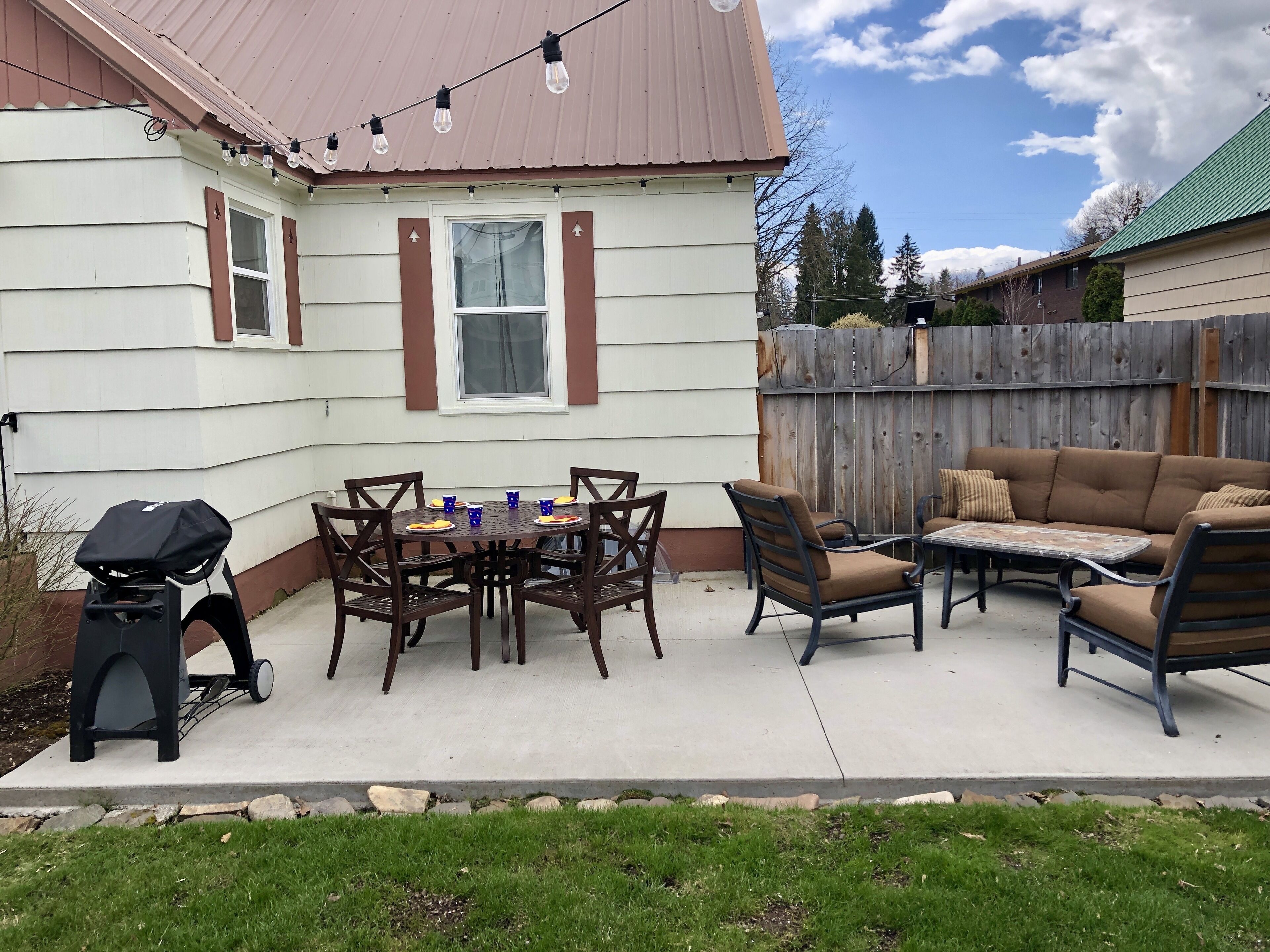 A patio with a table, chairs, a grill, and a wooden fence.