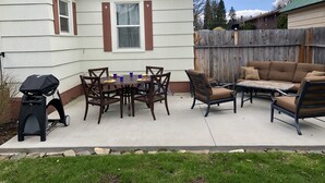 Un patio con mesa, sillas, una parrilla y un cerco de madera.