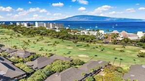 An aerial view of a golf course with a pool, surrounded by residential buildings and a view of the ocean.