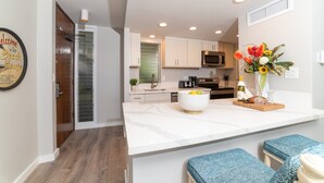 A modern kitchen with white cabinets, a large island with a bowl of lemons, and a microwave.