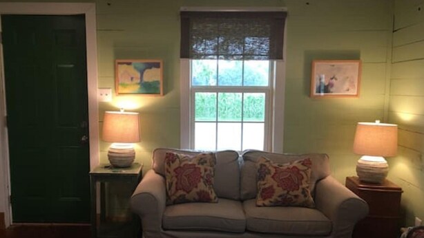 A living room with a sofa, two lamps, a window, and a door.