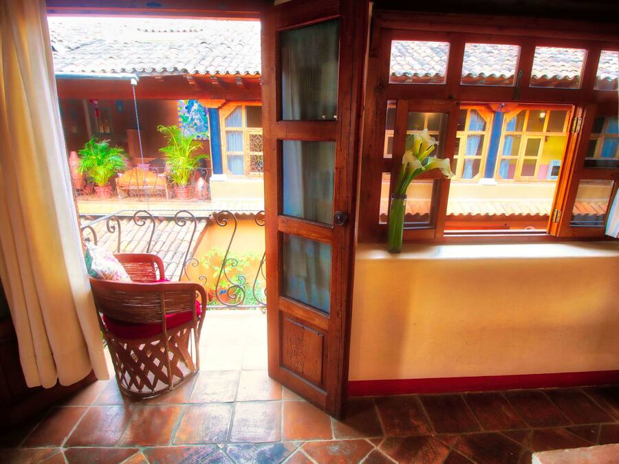 Une pièce avec une porte en bois donnant sur un balcon agrémenté de plantes en pot et d’une chaise en osier.