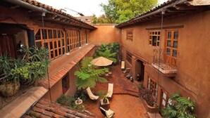 A courtyard with terracotta-roofed buildings, a central seating area with a table and chairs, and lush greenery. - Casa Encantada (Patzcuaro)