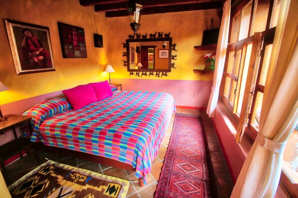 Une chambre avec un lit, une table de chevet, une lampe, un miroir et une fenêtre avec des rideaux.
