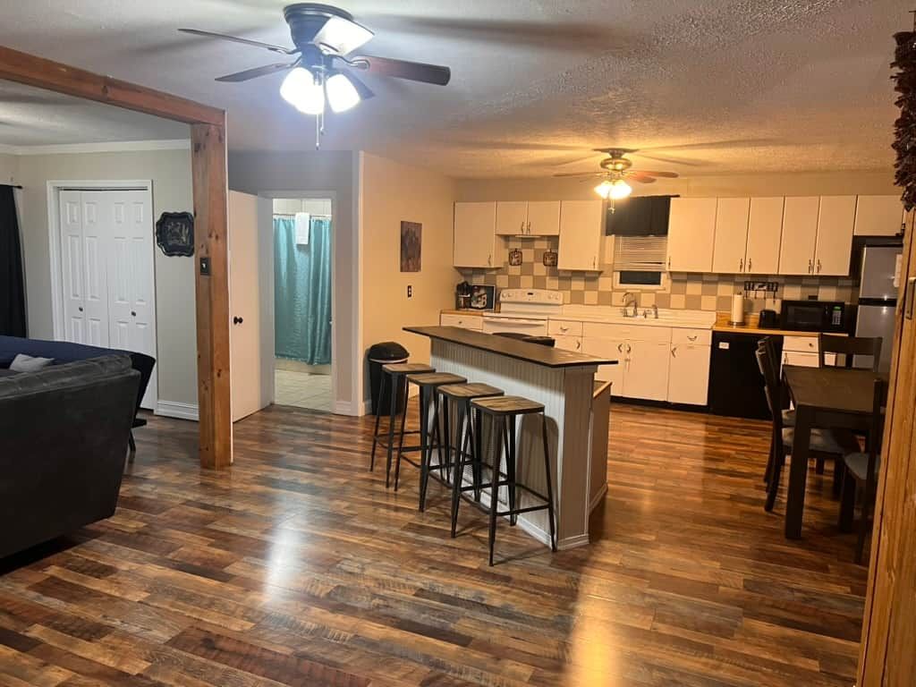 A kitchen with a bar area, wooden flooring, and a ceiling fan.