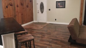 A room with a wooden floor, a white door, a framed picture on the wall, and a brown couch. - Coal Miner's Cabin - Near Winterplace, Beckley and Princeton (Shady Spring)