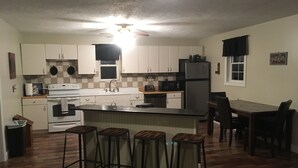 A compact kitchen with white cabinets, a black refrigerator, a microwave, and a stove. There are four stools at the kitchen island. - Coal Miner's Cabin - Near Winterplace, Beckley and Princeton (Shady Spring)