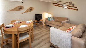 Un salon chaleureux avec une table à manger en bois, mise pour quatre personnes, un canapé et un téléviseur.