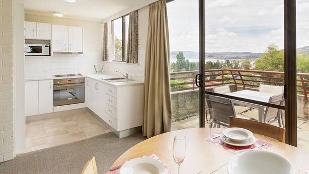 Une cuisine moderne avec des meubles blancs et un four à micro-ondes, un coin repas avec une table dressée pour deux personnes, et un balcon offrant une vue sur le paysage.