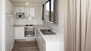Une cuisine compacte avec des meubles blancs, un four à micro-ondes encastré, une cuisinière et un évier.