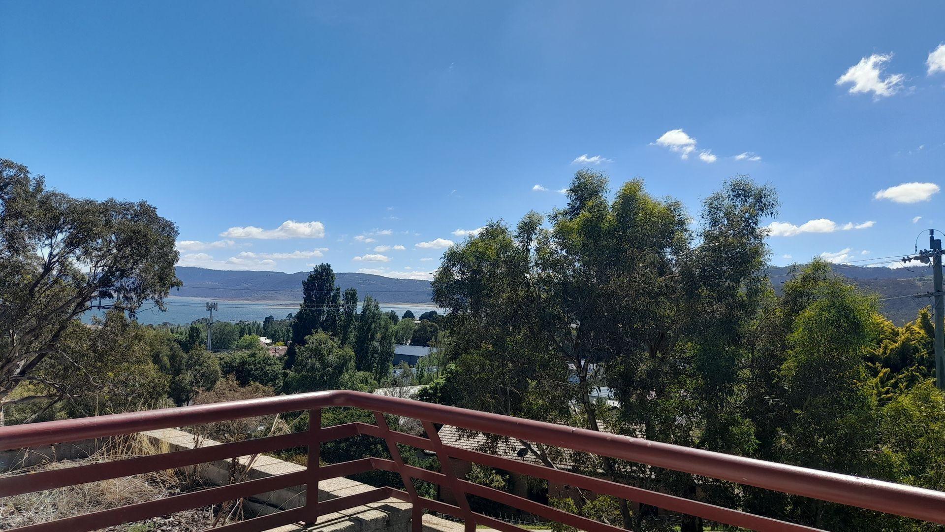 Vista desde un balcón con barandilla, sobre un cuerpo de agua, árboles y colinas distantes.