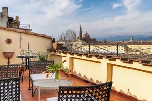 A terrace with outdoor seating, a vase with flowers, and a view of a cityscape with historic buildings. - Cellini Terrace - Florence (Firenze)