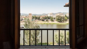 Blick vom Balkon auf einen Fluss mit Gebäuden und Bäumen im Hintergrund.