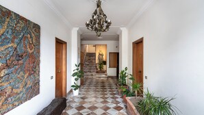 Ein Korridor mit Schachbrettfußboden, einer Holzbank, einem großen Mosaikbild und einer Treppe zu einem Raum mit einer Statue.
