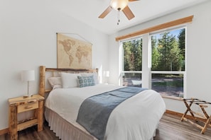 Una camera da letto con un letto, una testata in legno, una mappa del mondo, una finestra vista alberi e una ventola a soffitto.
