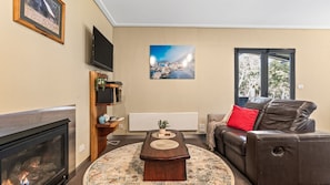 Un salon avec une cheminée, un canapé en cuir, une table basse, un téléviseur fixé au mur et un tableau.