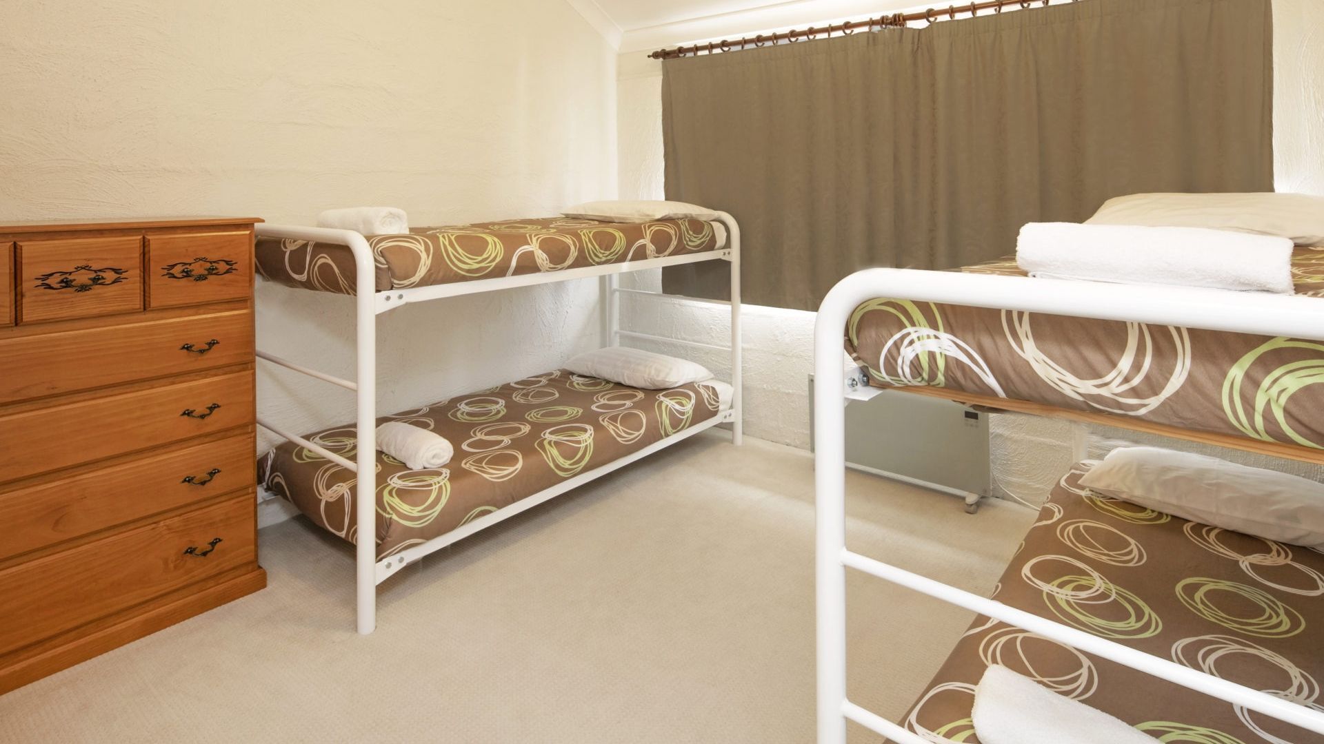 A room with bunk beds, a wooden dresser, and a window with curtains.