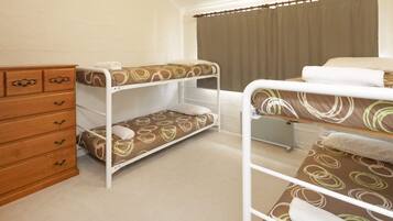 A room with bunk beds, a wooden dresser, and a window with curtains.