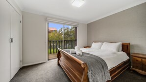A bedroom with a wooden bed, a nightstand, a wardrobe, and a sliding glass door to a balcony. - Petersdorf 2 - Modern 2BR Townhouse l WiFi l Mountain Views (Jindabyne)