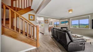 A spacious living area with a wooden staircase, a leather sofa, and a dining area with a view of the countryside. - Petersdorf 2 - Modern 2BR Townhouse l WiFi l Mountain Views (Jindabyne)