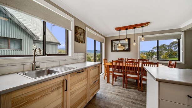 A modern kitchen with a large island, wooden cabinets, and a dining area with a wooden table and chairs. - Petersdorf 2 - Modern 2BR Townhouse l WiFi l Mountain Views (Jindabyne)