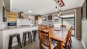 A modern kitchen with a central island, bar stools, and a dining table with chairs. - Petersdorf 2 - Modern 2BR Townhouse l WiFi l Mountain Views (Jindabyne)