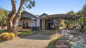 A modern building with a covered entrance, stone foundation, and a sign indicating 'Kickenback.com.au'. - Kickenback Lodge - 3BR Lodge l Gym l Indoor Pool l Tennis l WiFi l Air-Con (Crackenback)