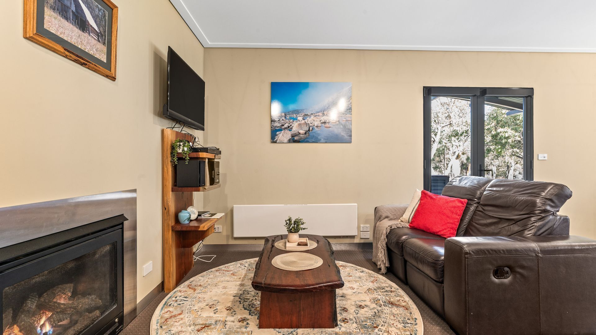 A living room with a fireplace, a leather sofa, a coffee table, a TV mounted on the wall, and a painting.