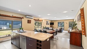 A modern kitchen with a central island, dining area with chairs, a sofa, and a TV. - Kickenback Lodge - 3BR Lodge l Gym l Indoor Pool l Tennis l WiFi l Air-Con (Crackenback)