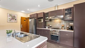 A modern kitchen with stainless steel appliances, a sink, and a countertop. - Kickenback Lodge - 3BR Lodge l Gym l Indoor Pool l Tennis l WiFi l Air-Con (Crackenback)