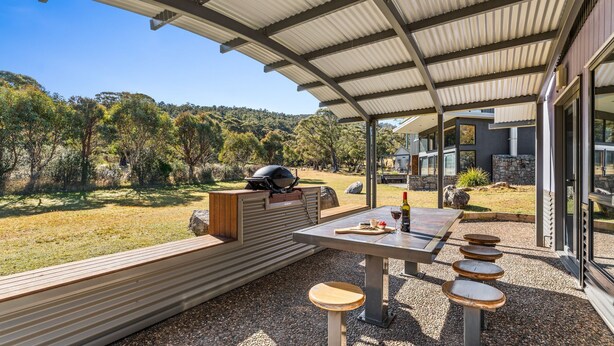 An outdoor patio with a grill, seating, and a table with wine glasses. - Kickenback Lodge - 3BR Lodge l Gym l Indoor Pool l Tennis l WiFi l Air-Con (Crackenback)
