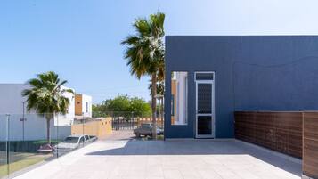 A modern building with a blue exterior, a gated entrance, and a paved patio area with palm trees.