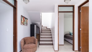 A hallway with a staircase, a leopard-print armchair, and a bed in the background.