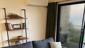 Uma sala de estar moderna com um sofá cinzento, uma mesa de centro de madeira, uma estante e uma porta de correr de vidro para o exterior.