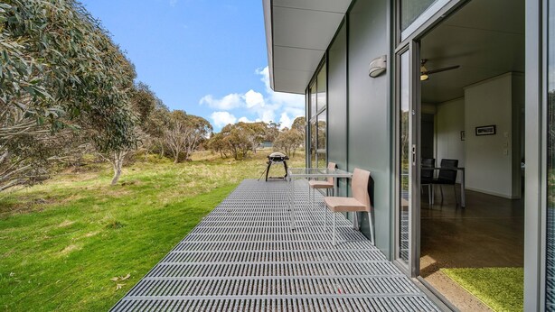 A modern outdoor patio with a metal grill, a table with chairs, and a glass door leading to an interior space. - Ecocrackenback 2 'Sustainable chalet close to the slopes.' (Crackenback)