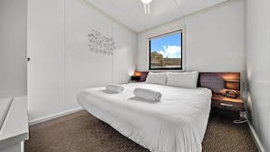 A modern hotel room with a large bed, a nightstand, a desk, and a window with a view of the outdoors. - Ecocrackenback 2 'Sustainable chalet close to the slopes.' (Crackenback)