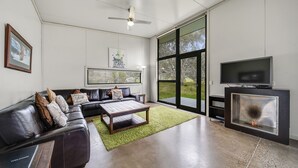 A modern living room with a leather sofa, a coffee table, a TV, and a fireplace. - Ecocrackenback 2 'Sustainable chalet close to the slopes.' (Crackenback)