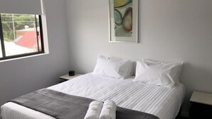 Ein Hotelzimmer mit einem großen Bett, weißen Kissen, einer grauen Decke und einem gerahmten abstrakten Gemälde an der Wand.