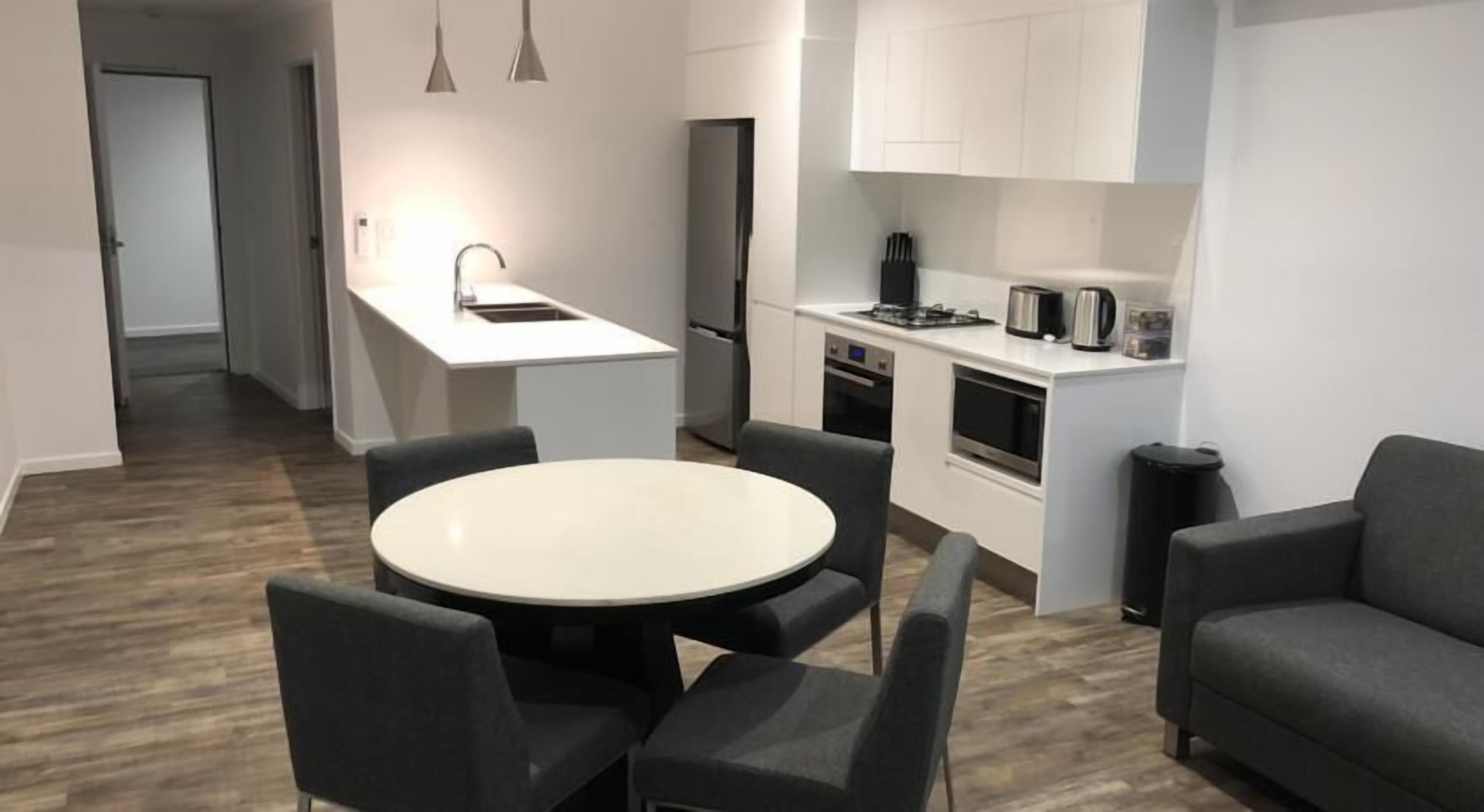 A modern kitchen with white cabinets, a central island with a sink, and a dining area with a round table and four chairs.