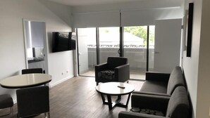 Ein modernes Wohnzimmer mit einer Couch, zwei Sesseln, einem kleinen runden Tisch und einem an der Wand befestigten Flachbildfernseher.