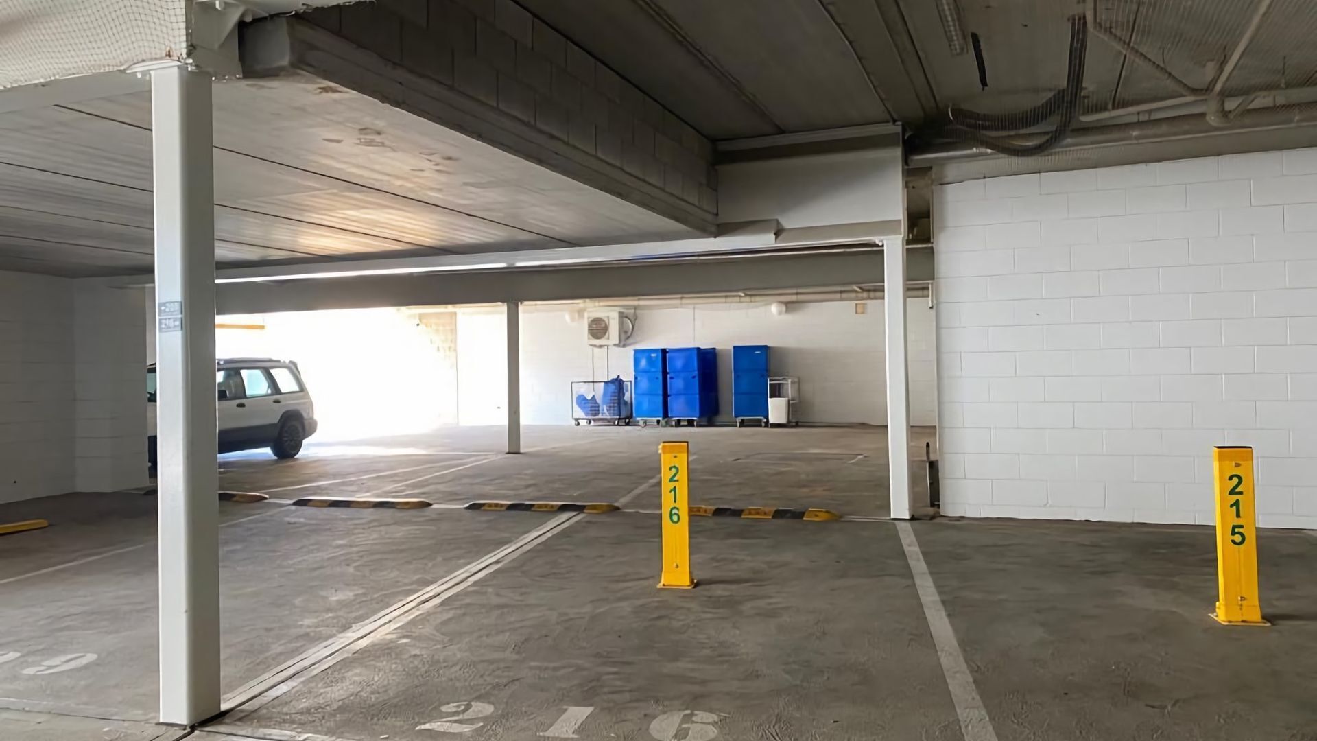 A parking garage with concrete floors, white walls, and a white car parked in the distance.