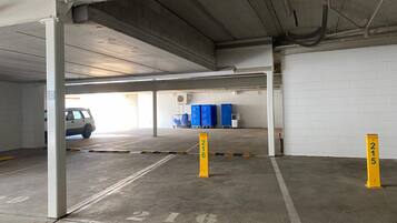 A parking garage with concrete floors, white walls, and a white car parked in the distance.